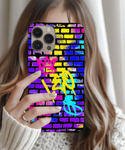 A bold phone case featuring vibrant graffiti-style “LEO” lettering in yellow, with a pink crown and teal symbol on a colorful brick wall background in neon blue, purple, and yellow tones.