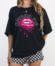 A woman wearing a black oversized t-shirt featuring the words “Libra AF” in bold curved text above glossy dripping pink lips, combining zodiac attitude with flirty glam style.