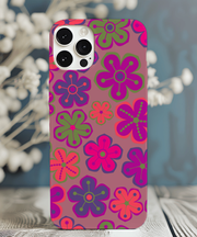 Phone case with a 70s-inspired retro flower pattern featuring bold pink, purple, green, and orange daisy shapes on a mauve background. The colorful floral design has a playful, groovy aesthetic perfect for vintage lovers.