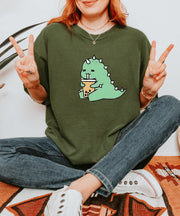 A cute green t-shirt featuring an adorable cartoon dinosaur happily sipping boba tea, creating a fun and cozy aesthetic perfect for casual or kawaii style lovers.