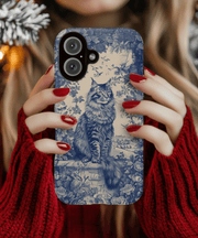 A tough phone case featuring an elegant navy blue toile de jouy illustration of a regal Maine Coon cat sitting among detailed floral patterns and vintage countryside scenery on a cream background.