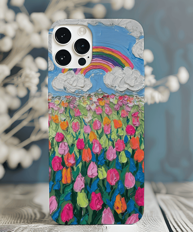 Phone case featuring a textured oil painting design of a vibrant tulip field under a blue sky with fluffy white clouds and a rainbow. The colorful brushstroke pattern in pink, orange, and green creates a cheerful, artistic spring aesthetic.