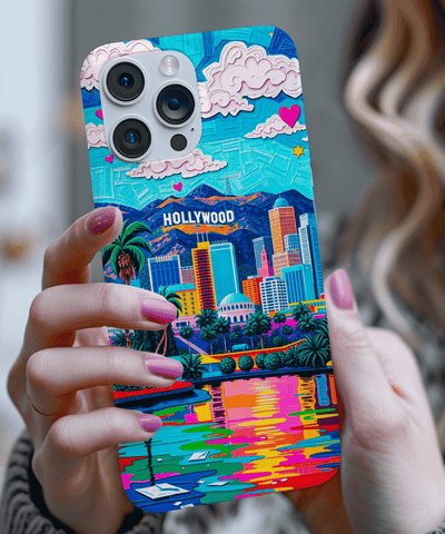A vibrant phone case showcasing a colorful Hollywood skyline with palm trees, skyscrapers, mountains, pink hearts, and a glowing sunset reflection in rainbow tones. The design radiates retro California vibes.