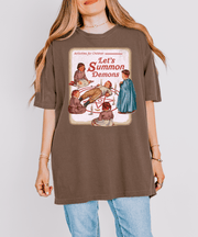 A brown oversized t-shirt featuring a retro children’s book-style illustration of kids gathered around a summoning circle with the phrase “Let’s Summon Demons” in vintage red text, parodying wholesome 80s design aesthetics.
