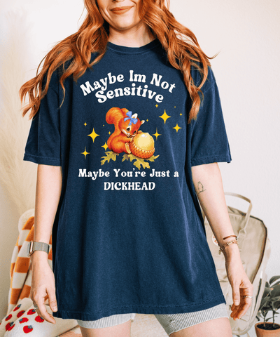 A navy oversized t-shirt featuring a vintage-style cartoon squirrel holding a giant acorn with sparkles around it. The shirt reads “Maybe I’m Not Sensitive, Maybe You’re Just a Dickhead” in playful white text.