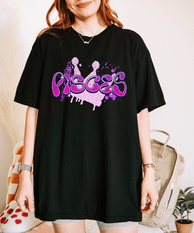 Black oversized t-shirt with the word “Pisces” in a purple graffiti-style drip font and ink-splatter accents. The design gives off a bold, artsy zodiac vibe perfect for astrology lovers and those with a creative, dreamy edge.