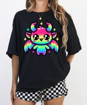 Black oversized t-shirt featuring a cute kawaii Baphomet character with rainbow wings, striped rainbow body, colorful horns, and sparkly stars. Bright, pastel goth design mixing adorable chaos and pride energy.