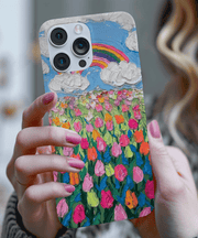 Phone case featuring a textured oil painting design of a vibrant tulip field under a blue sky with fluffy white clouds and a rainbow. The colorful brushstroke pattern in pink, orange, and green creates a cheerful, artistic spring aesthetic.