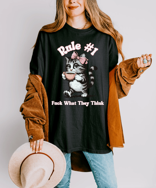 Black oversized t-shirt featuring a retro-style cat with a pink bow holding a teacup and bold text that reads “Rule #1: Fuck What They Think.” Perfect for confident, independent women who love sarcastic humor, vintage cat art, and statement fashion.