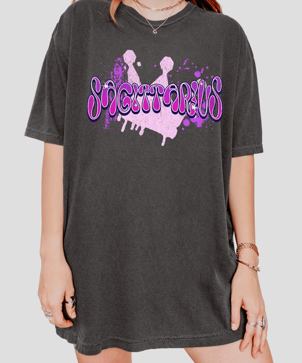 Pepper gray oversized t-shirt with the word “Sagittarius” in bold pink and purple airbrush-style bubble letters over a paint splatter background. Perfect for astrology lovers and Sagittarius signs who love edgy, vibrant, streetwear-inspired designs.