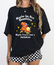 A black oversized t-shirt featuring a vintage-style cartoon squirrel holding a giant acorn with sparkles around it. The shirt reads “Maybe I’m Not Sensitive, Maybe You’re Just a Dickhead” in playful white text.