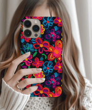 Phone case with a black background covered in vibrant neon embroidered-style flowers in pink, blue, yellow, orange, green, and purple. The colorful design mimics stitched thread for a textured, bold, and artistic look.