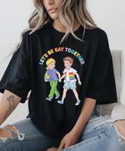 A black oversized t-shirt with a vintage-style illustration of two kids holding hands, one wearing a rainbow-striped shirt, and the phrase “Let’s Be Gay Together” in colorful retro lettering above them.